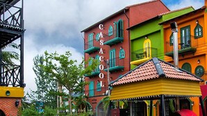 Un espacio al aire libre con mesas y sillas, una parrilla y edificios coloridos al fondo.