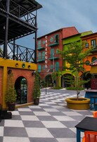 A colorful courtyard with a checkered floor, a building with a sign reading "CASA COOL", and potted plants.