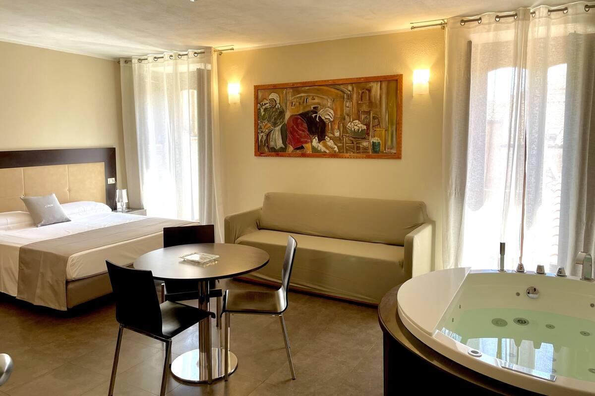 A hotel room with a bed, a sofa, a small table with chairs, a painting on the wall, and a bathtub.