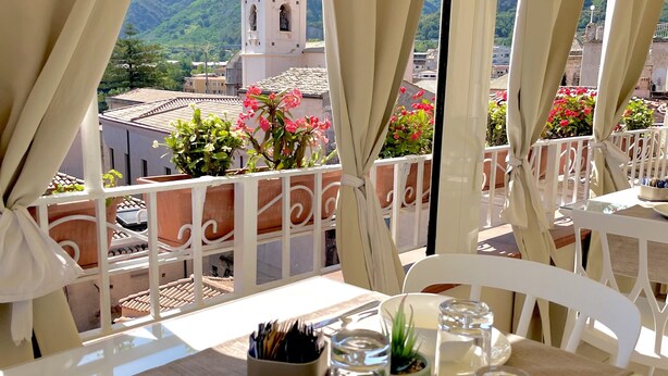 A dining table set for two with a view of a mountainous landscape and a church tower. - Residenza il Barone (Tropea)