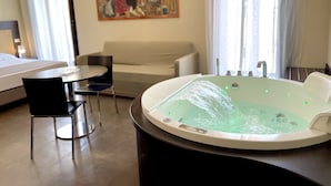 A hotel room with a large bathtub, a sofa, a dining table, and a painting on the wall. - Residenza il Barone (Tropea)