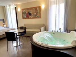 Habitación de hotel con una bañera grande, un sofá, una mesa de comedor y un cuadro en la pared.
