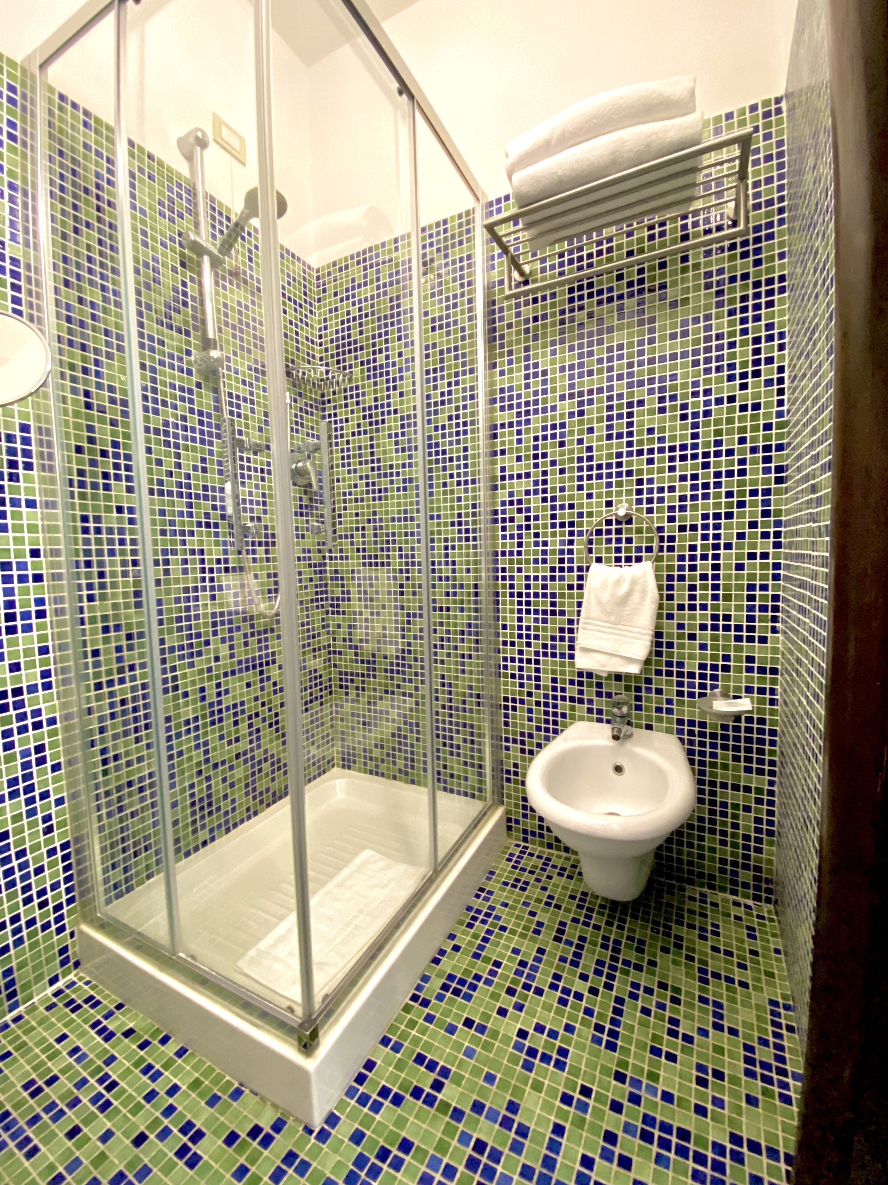 Een badkamer met een douchecabine van glas, een wastafel en mozaïek vloertegels.