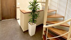 A spiral staircase with a wooden finish, a potted plant, and a door in a hallway with tiled flooring. - Residenza il Barone (Tropea)