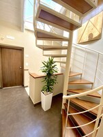 Una escalera de caracol con detalles de madera, una planta en maceta y una puerta en un pasillo con suelo de baldosas.