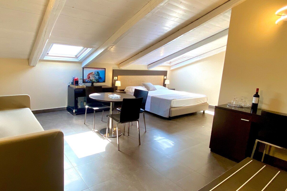 A compact hotel room with a bed, a desk with a computer, a chair, and a couch.