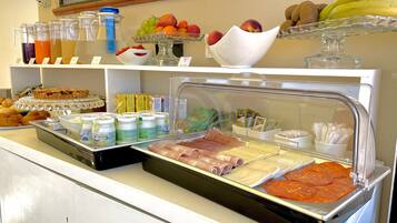 A buffet with various food items including fruits, juices, and deli meats.