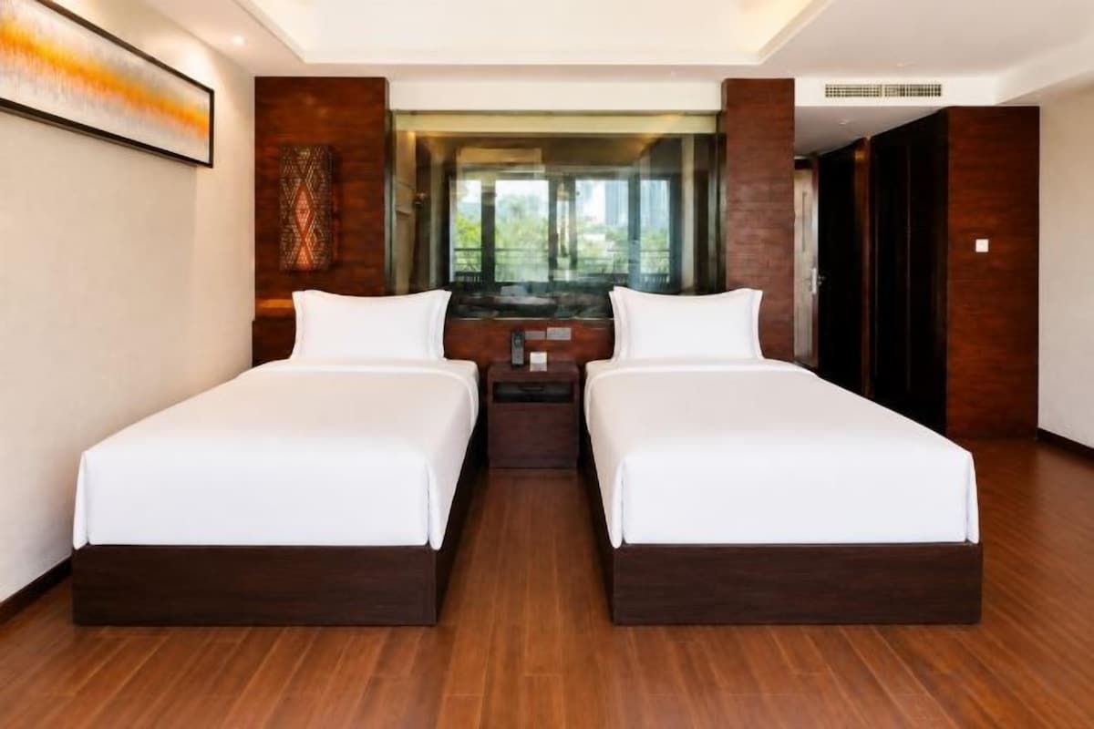 A hotel room with two single beds, a large window, and a view of greenery.