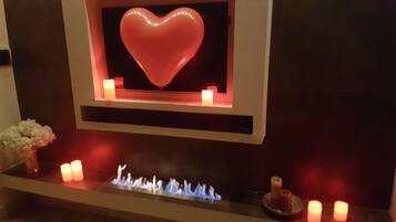 A fireplace with a heart-shaped light, candles, and a small plant.