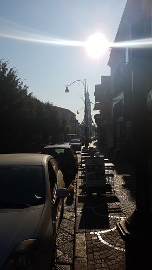 Eine gepflasterte Straße mit parkenden Autos und Außenbestuhlung.