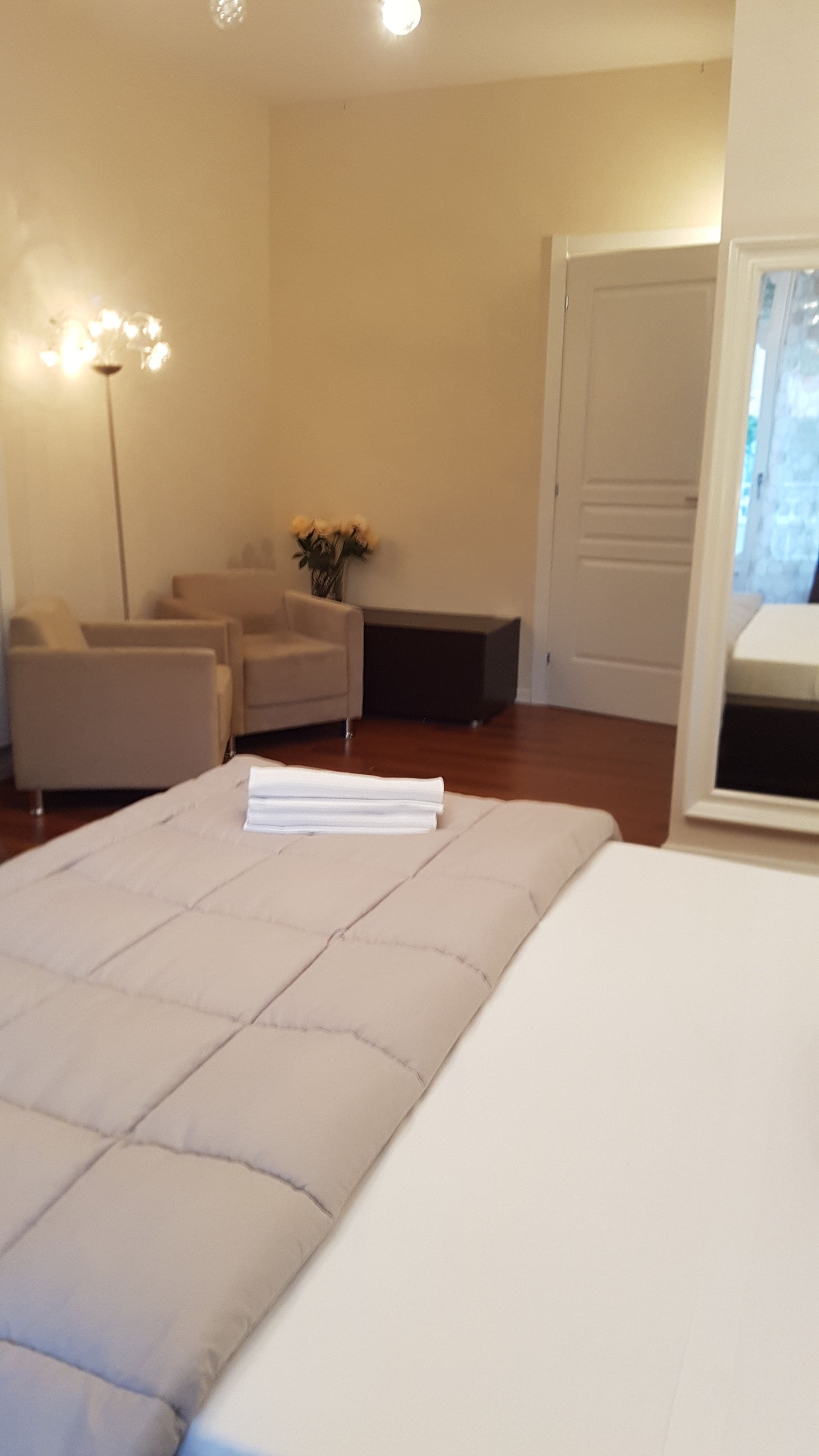 Een slaapkamer met een groot bed, een bank, een stoel, een bijzettafeltje met bloemen en een deur.