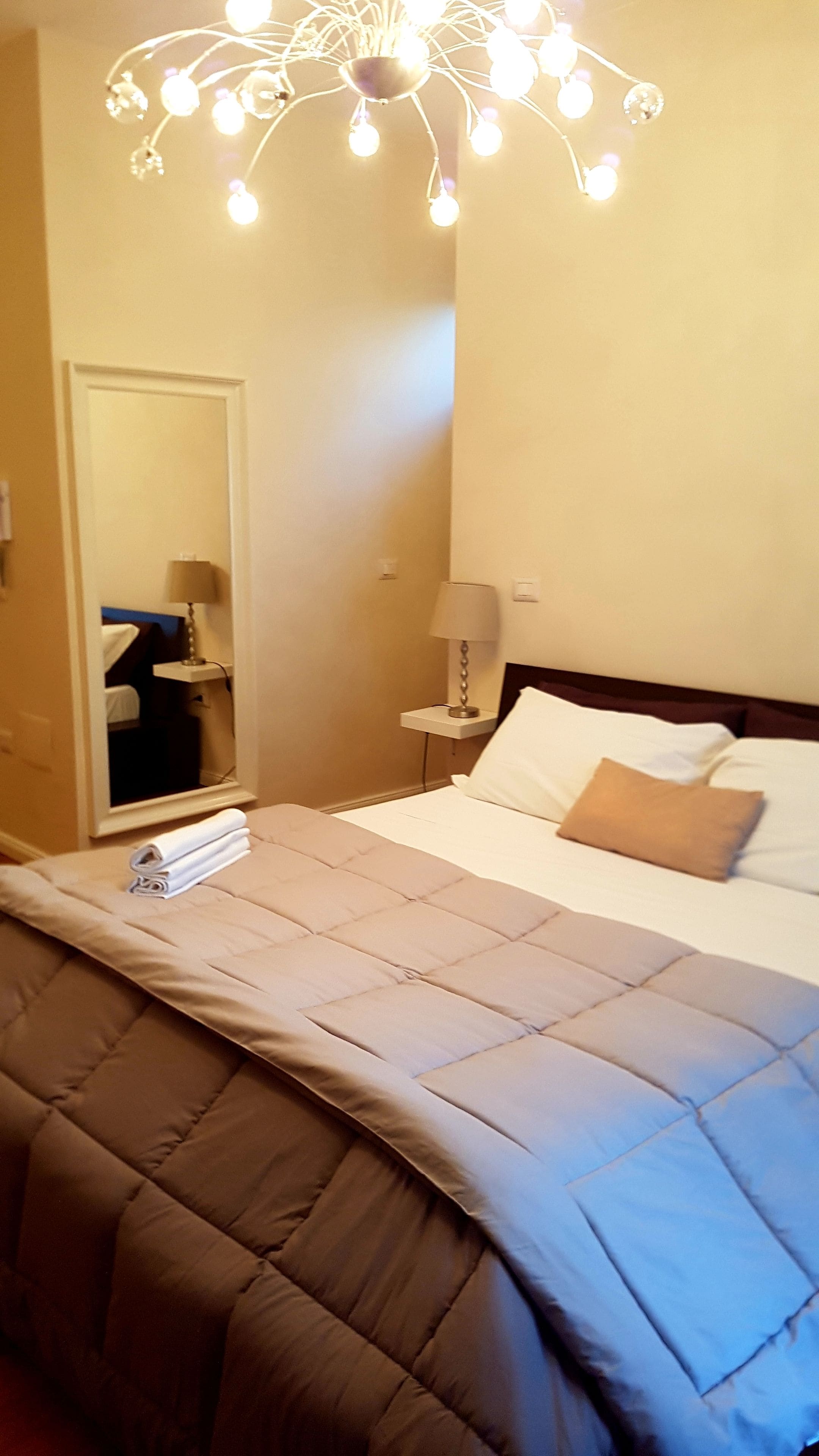 A hotel room with a bed, a nightstand, a lamp, and a mirror.