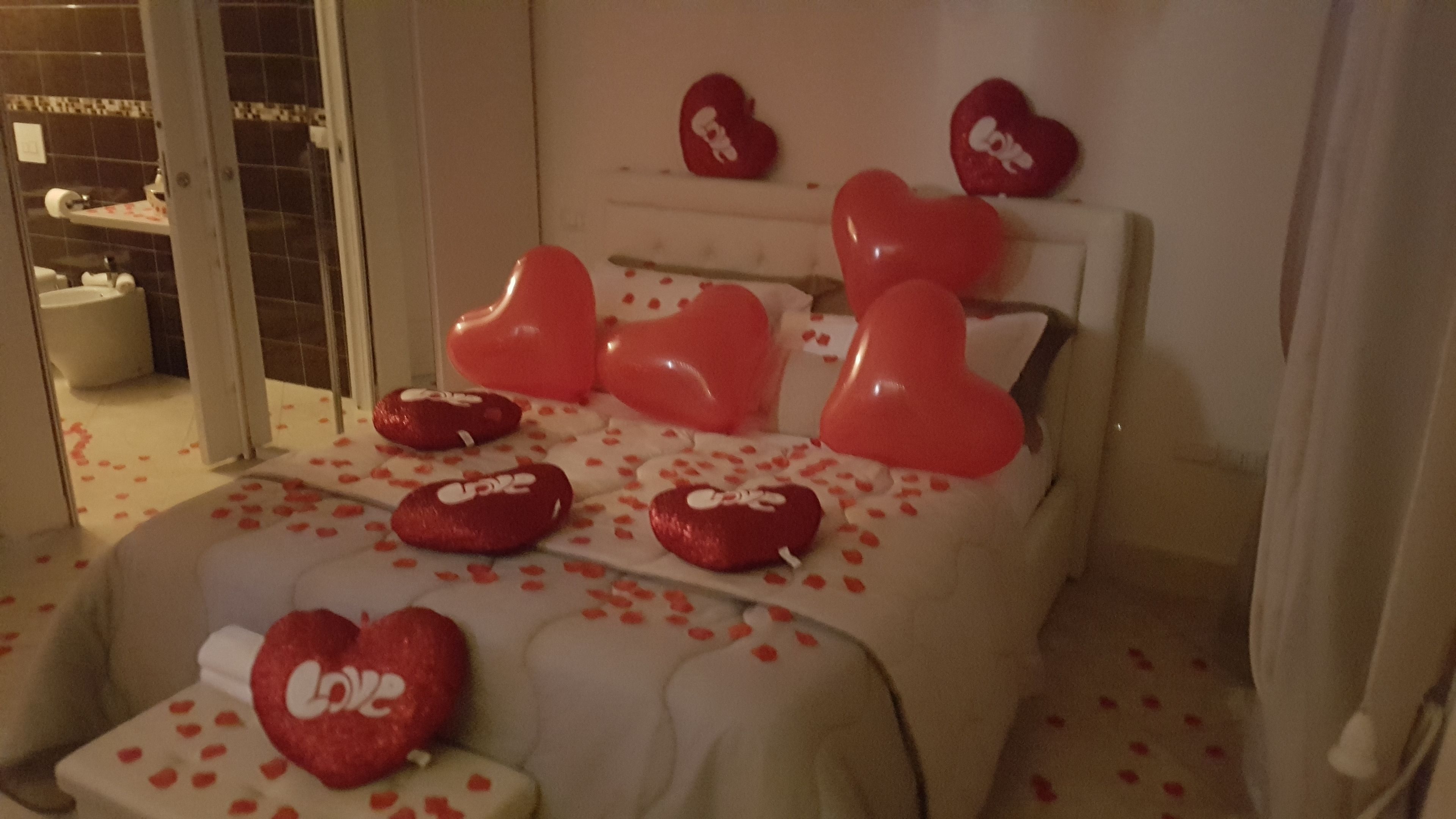 A hotel room with a bed adorned with red heart-shaped pillows and a heart-shaped pillow on the bedside table.