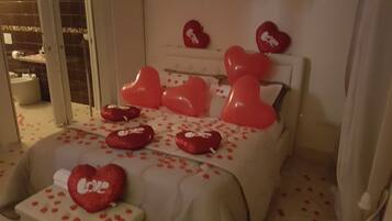A hotel room with a bed adorned with red heart-shaped pillows and a heart-shaped pillow on the bedside table.