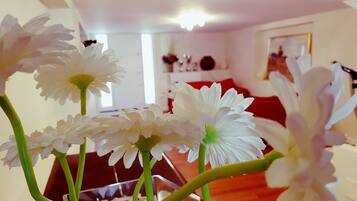 Una habitación con un florero de vidrio con flores blancas sobre una mesa, un sofá rojo y un cuadro en la pared.