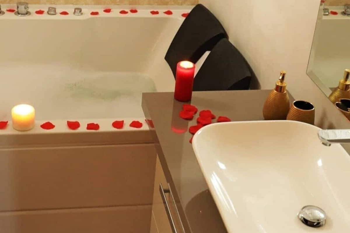 Une salle de bain avec une baignoire, un lavabo et un miroir. Des pétales de rose et des bougies sont disposés sur le bord de la baignoire.