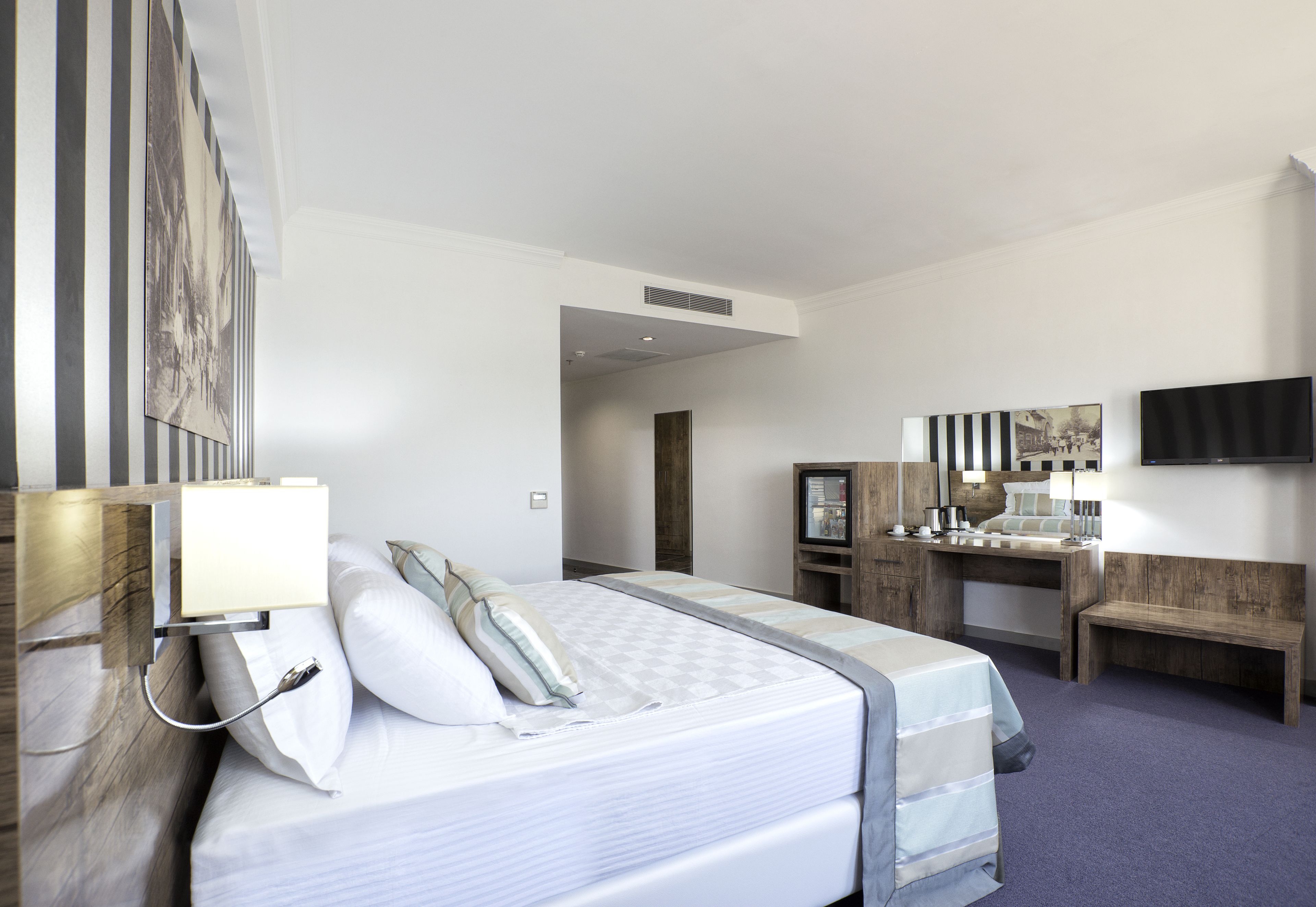 Habitación de hotel con cama, mesita de noche, lámpara, escritorio, silla y televisor en la pared.