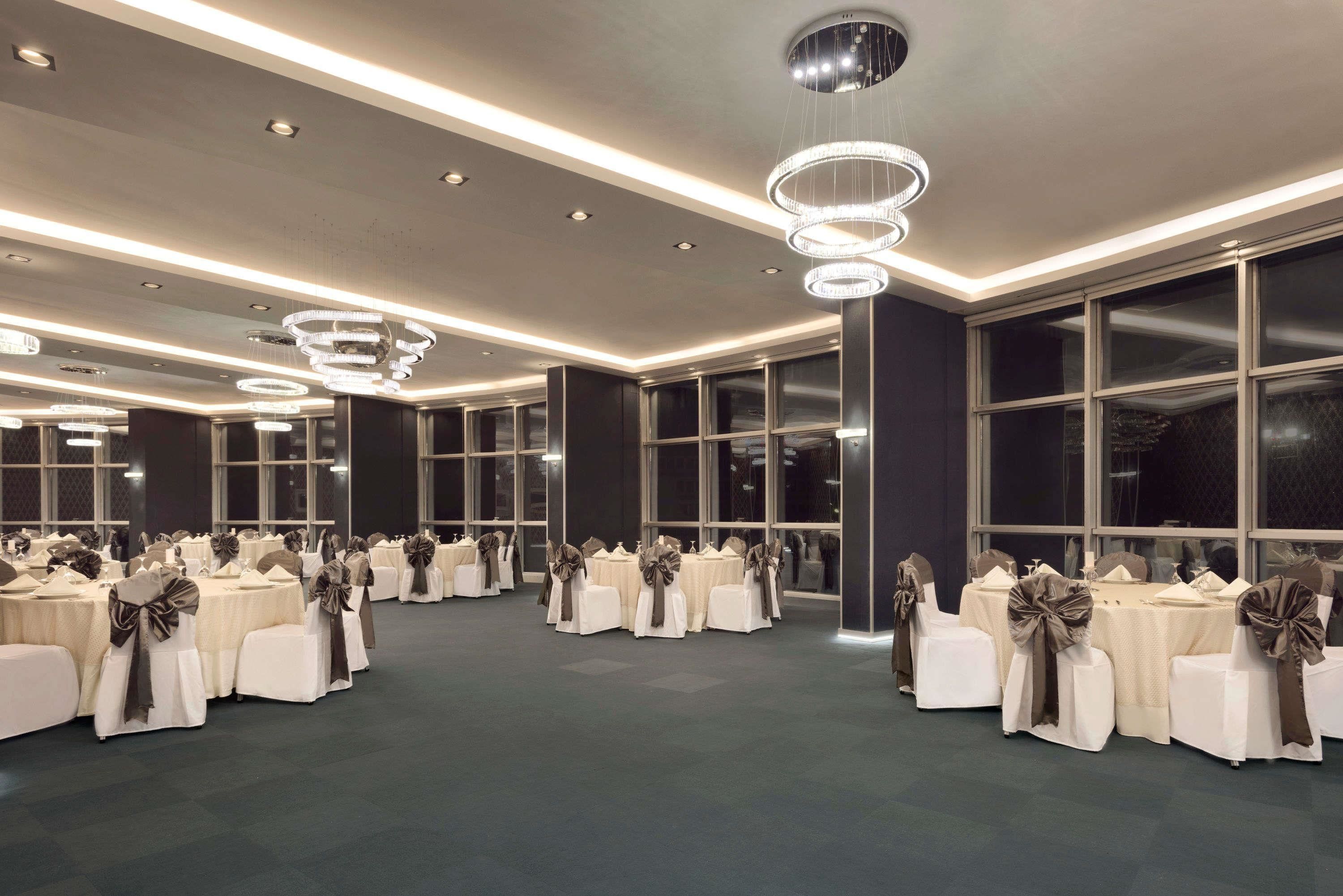 A large, well-lit banquet hall with multiple round tables, each adorned with white tablecloths and brown sashes.