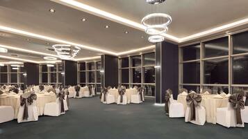 A large, well-lit banquet hall with multiple round tables, each adorned with white tablecloths and brown sashes.