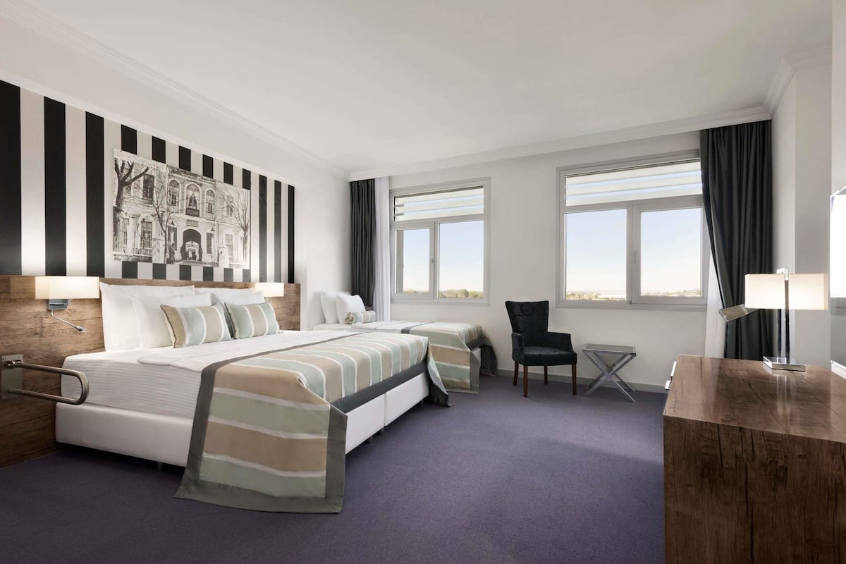 A hotel room with a large bed, two bedside tables, a chair, a small table, and a painting on the wall.