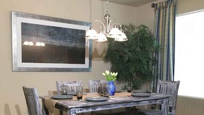 Ein Essbereich mit Holztisch, Stühlen, einer Bank, einer Pendelleuchte, einem gerahmten Bild und einem Blumentopf.