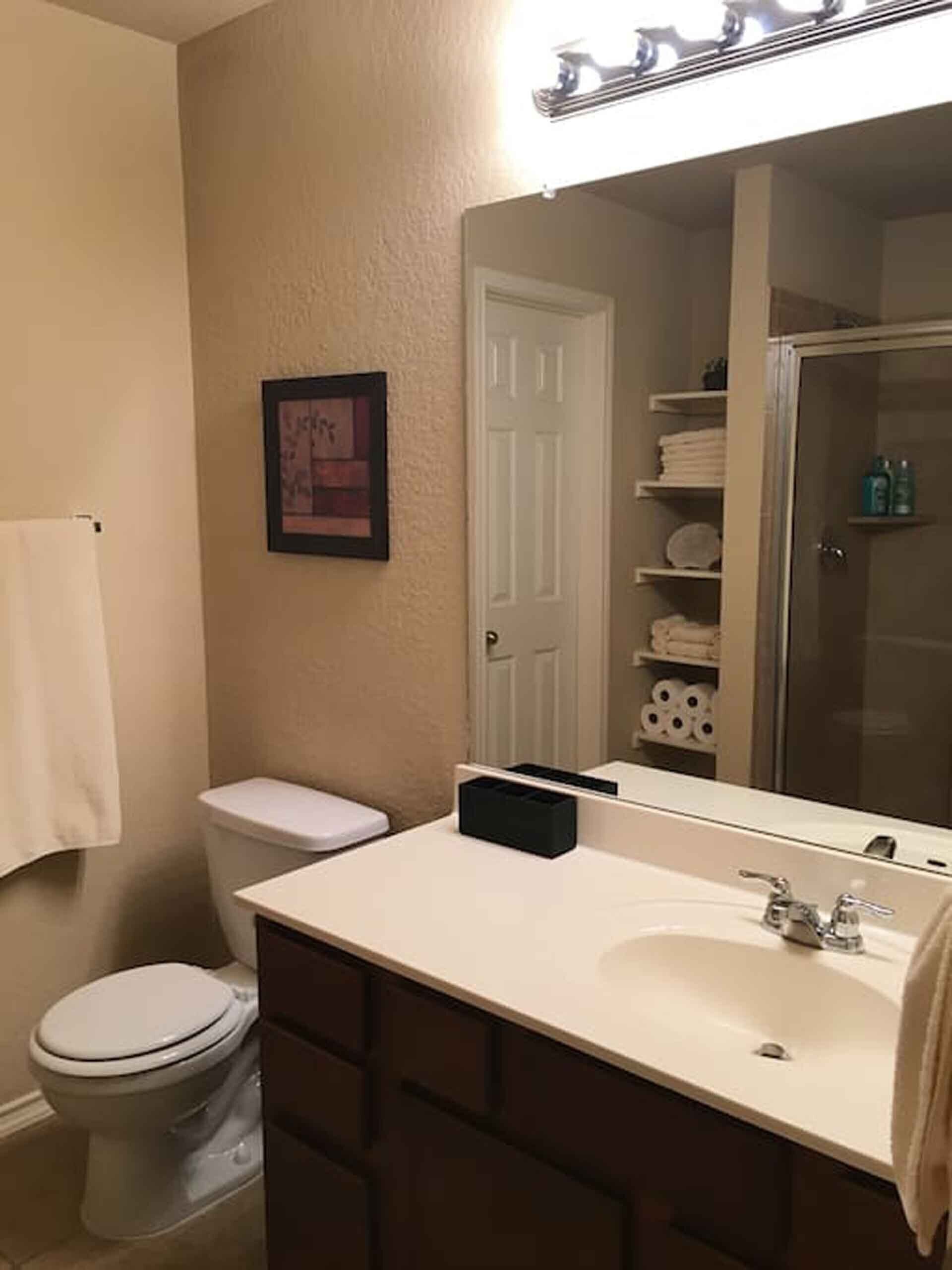 A bathroom with a white toilet, a sink with a mirror above it, and a towel hanging on the wall.