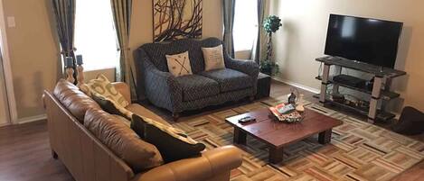 Un salon comprenant un canapé, une table basse, un téléviseur et un tapis à motifs.