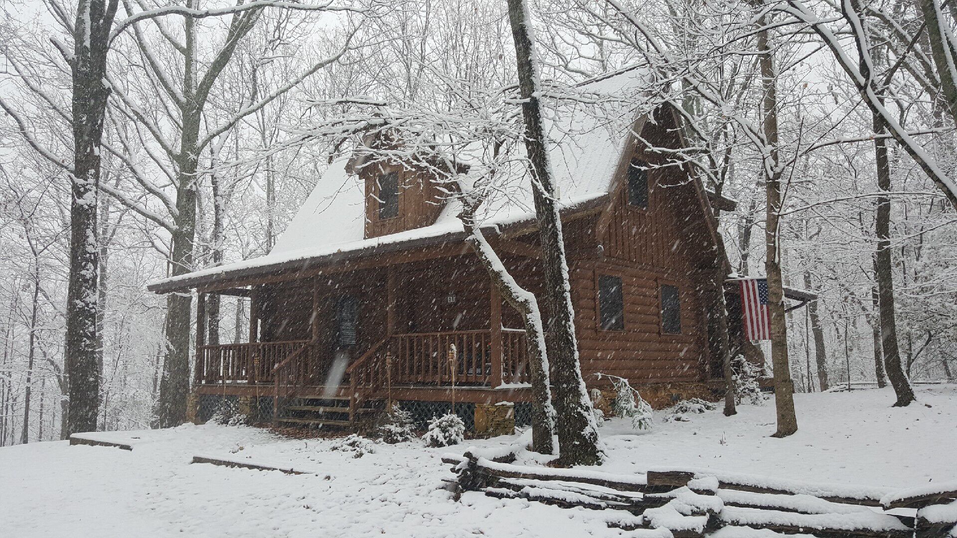 A wooden cabin with a porch, surrounded by snow-covered trees.