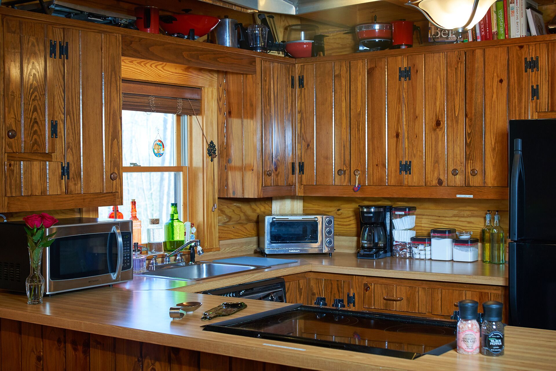 Una cocina con armarios de madera, microondas, horno tostador, cafetera y diversos utensilios de cocina.