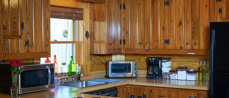 Una cocina con armarios de madera, microondas, horno tostador, cafetera y diversos utensilios de cocina.