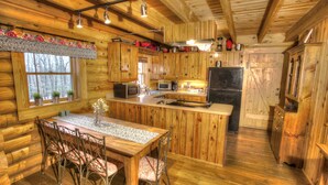 A wooden cabin interior with a kitchen, dining area, and a large window. - Sitting on 20 beautiful acres, totally secluded, Just 6 miles from Helen, GA! (Sautee Nacoochee)