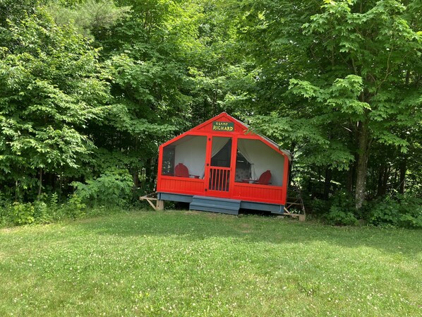 A red cabin named "GLAMP RICHARD" in a forested area with a grassy foreground.