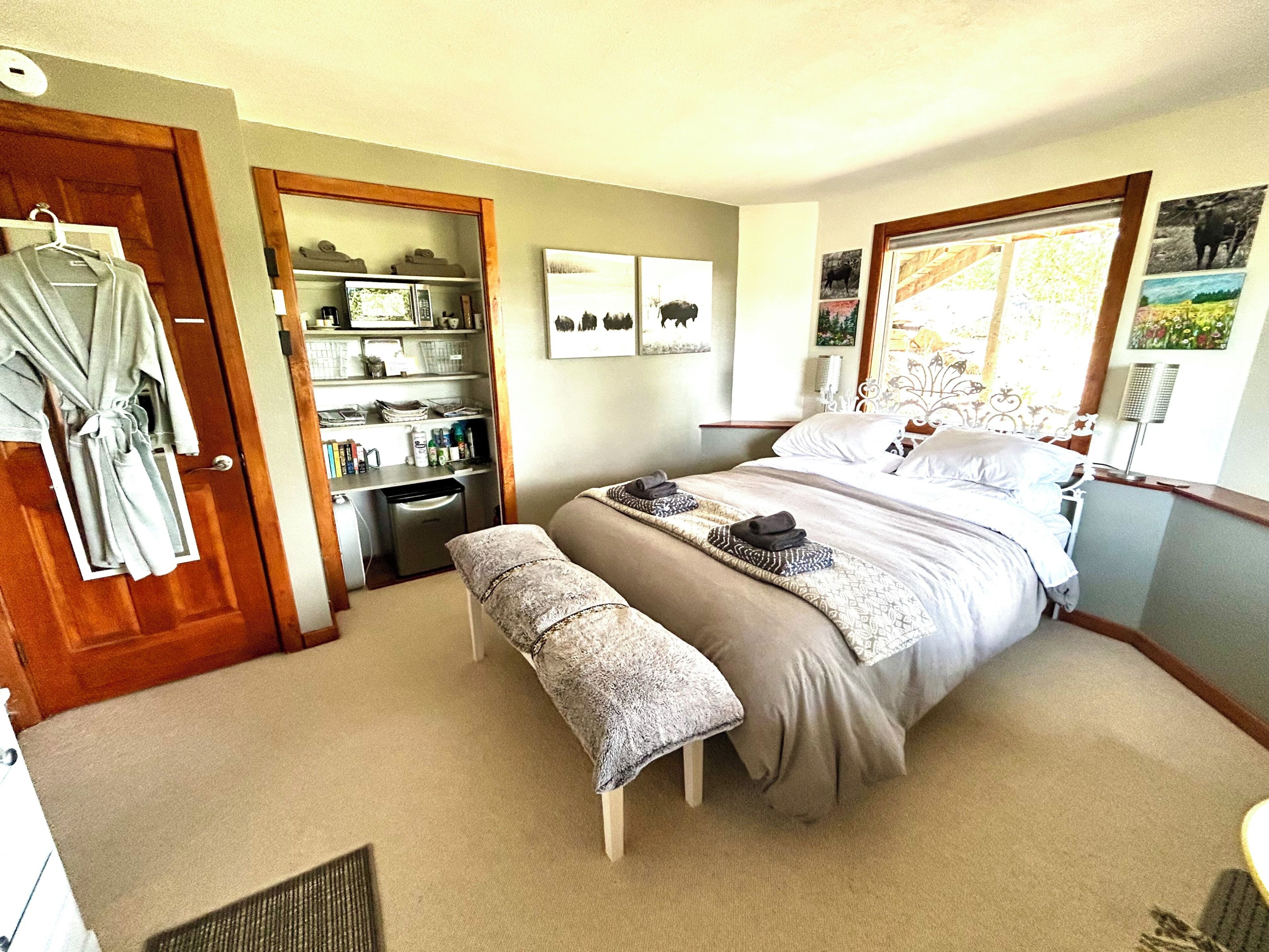 Un dormitorio con cama, un banco, un armario y una pequeña kitchenette.