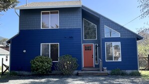 A two-story house with a red door, large windows, and a sloped roof. - No Host Fees! Lovely, well equipped, dog friendly home, 3 blocks from the beach! (Rockaway Beach)