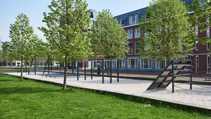 A playground with climbing structures and benches, surrounded by grass and trees, with a building in the background. - Great Family Loft apartment (Haarlem)