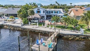 A waterfront property with a dock, lounge chairs, and a pool area. - The Boat House · Riverfront · Heated Pool & Spa · Tiki Bar · Sleeps 10 (Cape Coral)