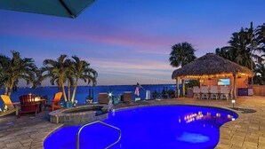 A pool area with lounge chairs, a bar, and a thatched-roof structure. - The Boat House · Riverfront · Heated Pool & Spa · Tiki Bar · Sleeps 10 (Cape Coral)