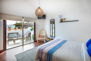 A bedroom with a bed, a chair, a sofa, a table, and a large window. - Villa with private Jacuzzi, pool and amazing sea views in a quiet area (Puerto del Carmen-La Asomada-Lanzarote)