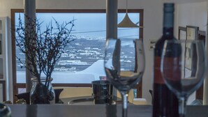 Een eetruimte met uitzicht op een kuststad, een vaas met takken en twee wijnglazen op tafel.