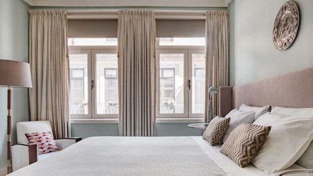 Une chambre d’hôtel avec un grand lit, une chaise, une table de chevet et une fenêtre avec des rideaux.