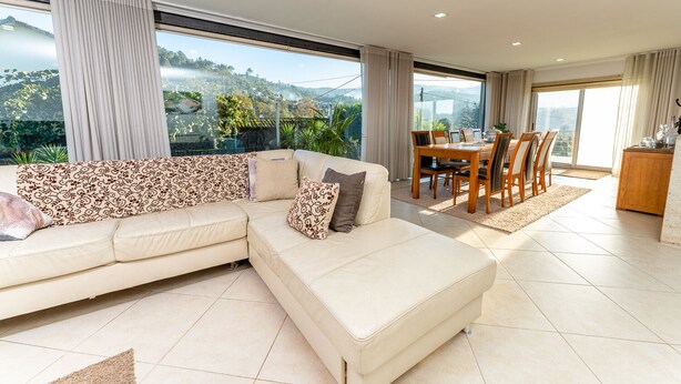 A modern living room with a large sectional sofa, a dining area with a wooden table and chairs, and large windows offering a view of a mountainous landscape. - Old house Alembic in Ponte de Lima (Ponte de Lima)