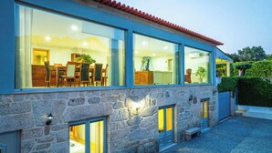 A stone building with large windows, a dining area visible inside, and a stone wall with a lantern. - Old house Alembic in Ponte de Lima (Ponte de Lima)