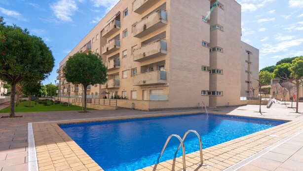 A swimming pool with a tiled deck, surrounded by a multi-story building with balconies.