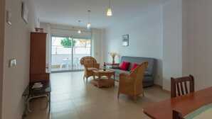 A living room with a sofa, chairs, a dining table, and a small kitchen area.