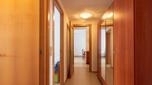 A hallway with wooden doors and a tiled floor, leading to a room with a bed and a chair.
