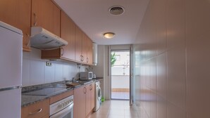 A modern kitchen with wooden cabinets, a built-in oven, a microwave, and a washing machine.