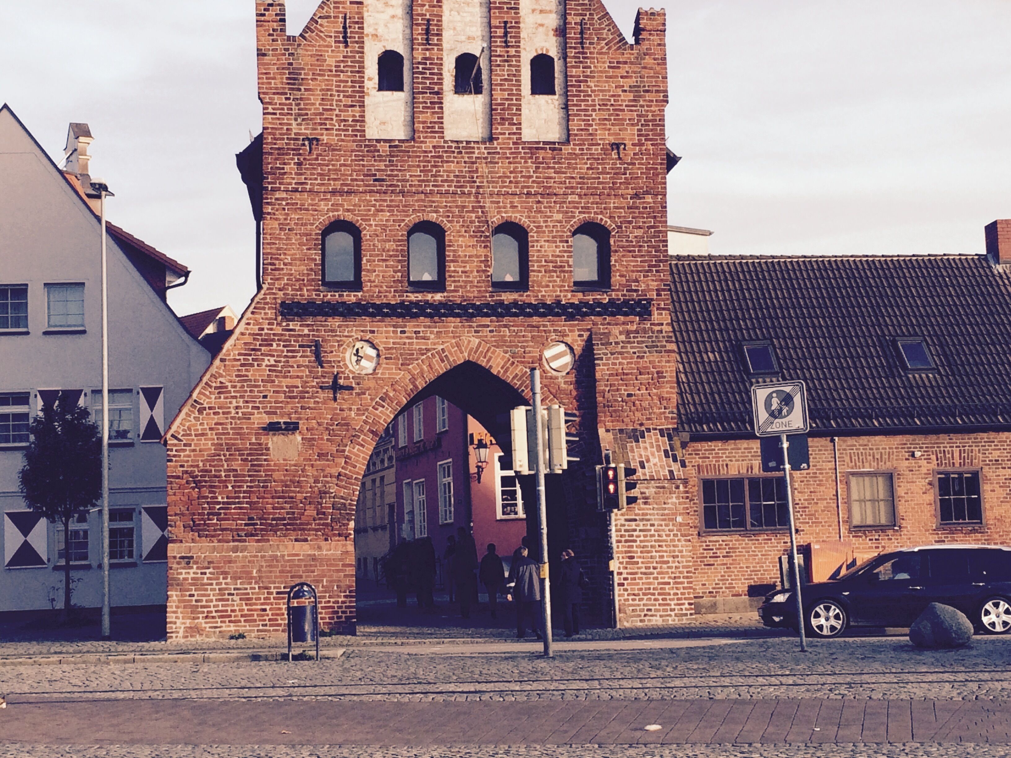 A historic brick building with a large arched entrance, a clock, and a "no parking" sign.