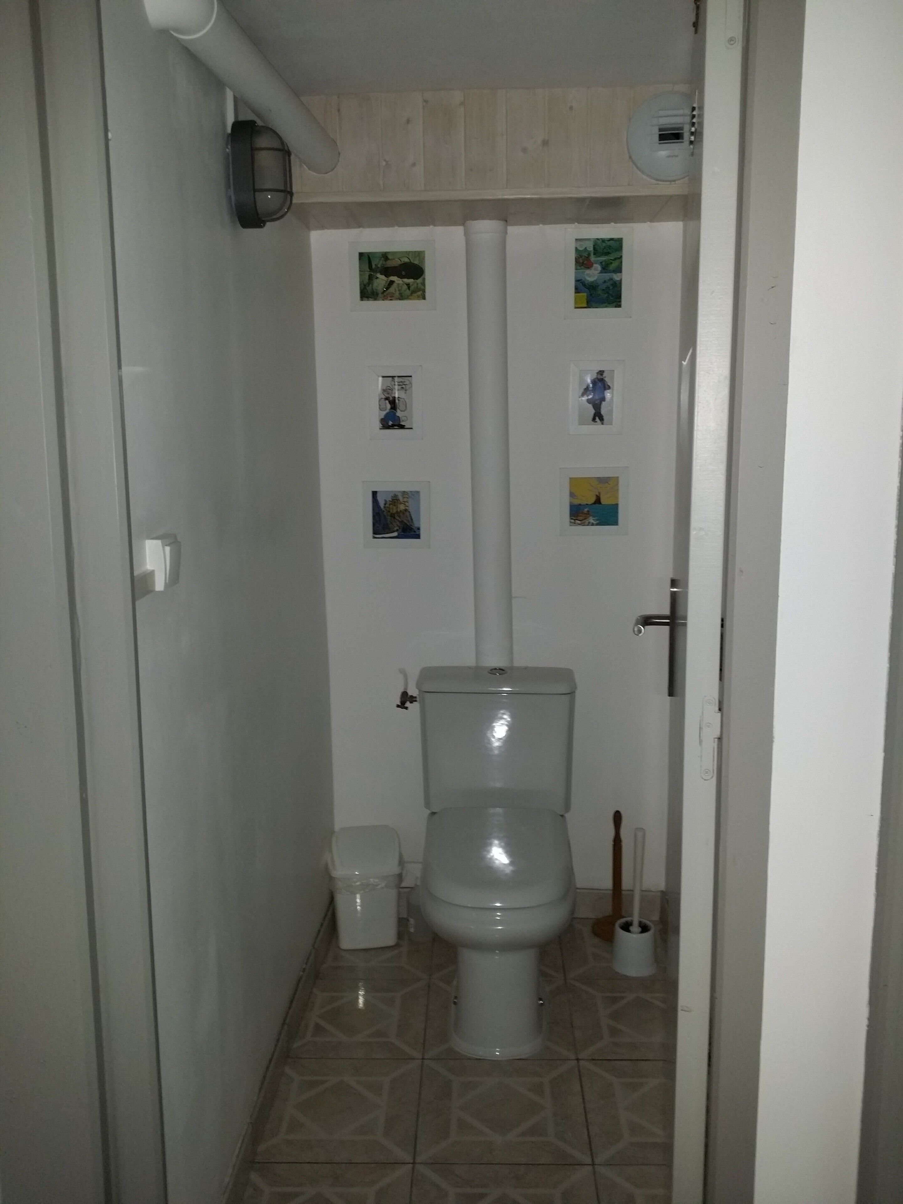 Een kleine, schone badkamer met toilet, prullenbak en toiletborstel.
