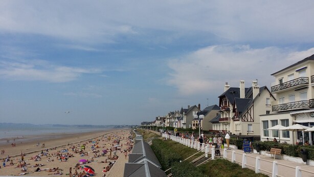 Une promenade en bord de mer bordée de maisons, une plage de sable et un ciel dégagé.