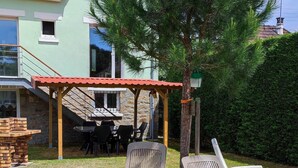 Une maison avec un toit recouvert de tuiles rouges, un patio abrité avec des meubles d’extérieur et une pelouse bien entretenue.